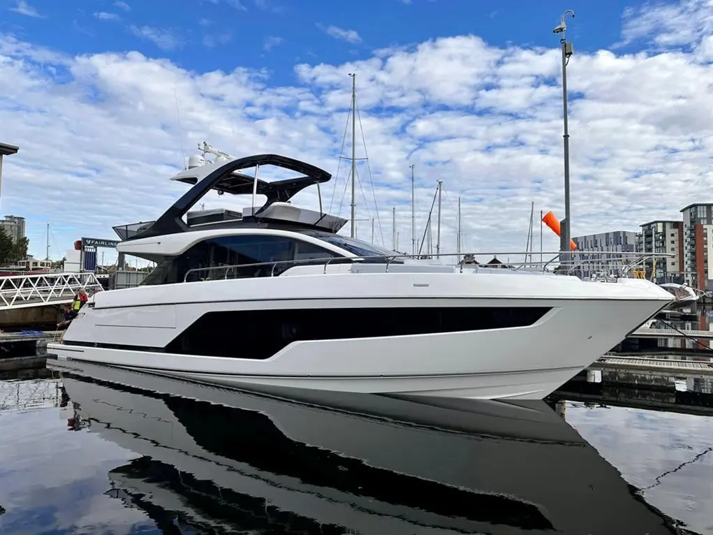 A sleek white yacht docked at a marina, reflecting on calm waters under a partly cloudy sky.